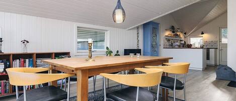 Uma sala de jantar com mesa e cadeiras de madeira, um tapete azul estampado e um claraboia acima.