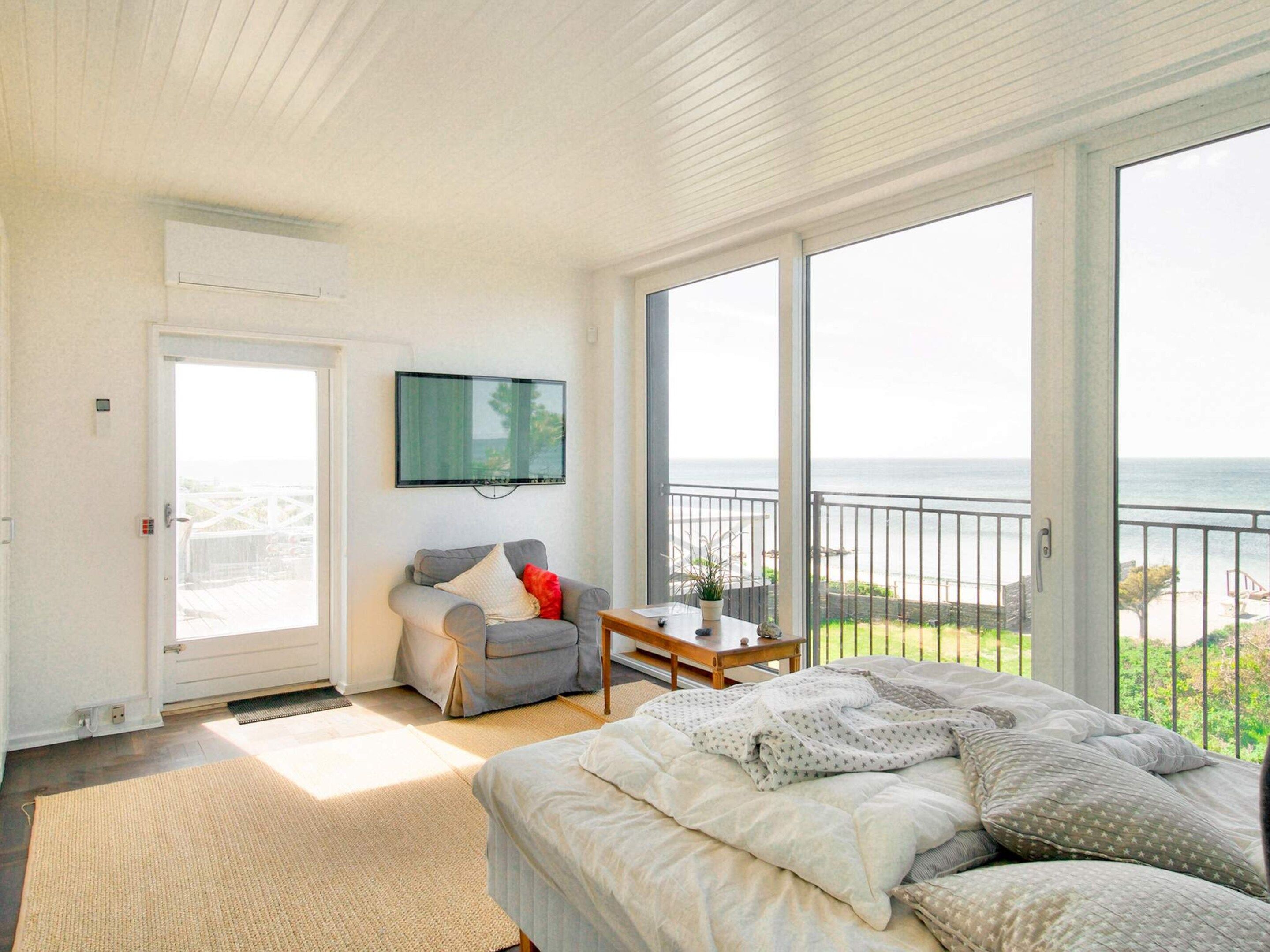 A bedroom with a bed, a TV, a chair, and a view of the ocean.