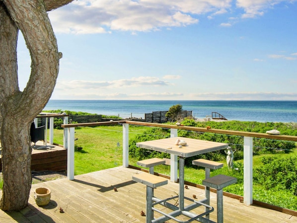 An outdoor deck with a view of the sea, a wooden table, and a bench. - 5 Star Holiday Home in Graested (Vejby)