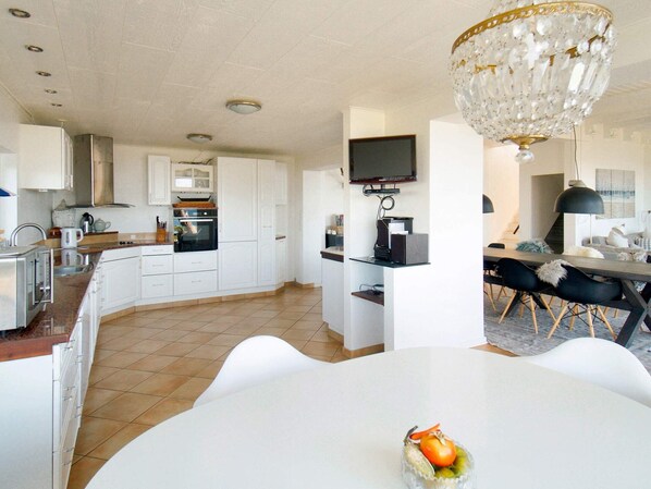 Une cuisine moderne avec des meubles blancs, un four encastré et un coin repas comprenant une table et des chaises blanches.