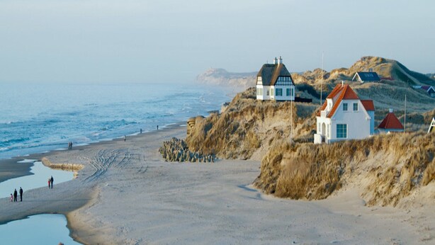 Une zone côtière avec une plage de sable, un petit plan d’eau et des maisons à l’architecture traditionnelle.
