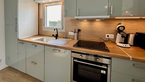 A modern kitchen with a built-in oven, a sink, and a window above the countertop. - 47 Reflets- 4p-wifi-parking-vue mer (Quiberon)