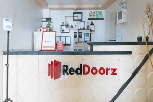 Un mostrador de recepción con el logotipo de RedDoorz, un certificado enmarcado y una cámara de seguridad.