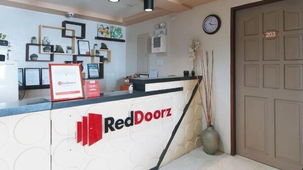 A reception desk with the RedDoorz logo, framed certificates, a clock, and a door marked with the number 203. - RedDoorz @ Bridgeway Hotel Tuguegarao City (Tuguegarao)