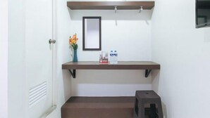 A bathroom with a white door, a mirror, a shelf with toiletries, and a small stool. - RedDoorz @ Bridgeway Hotel Tuguegarao City (Tuguegarao)