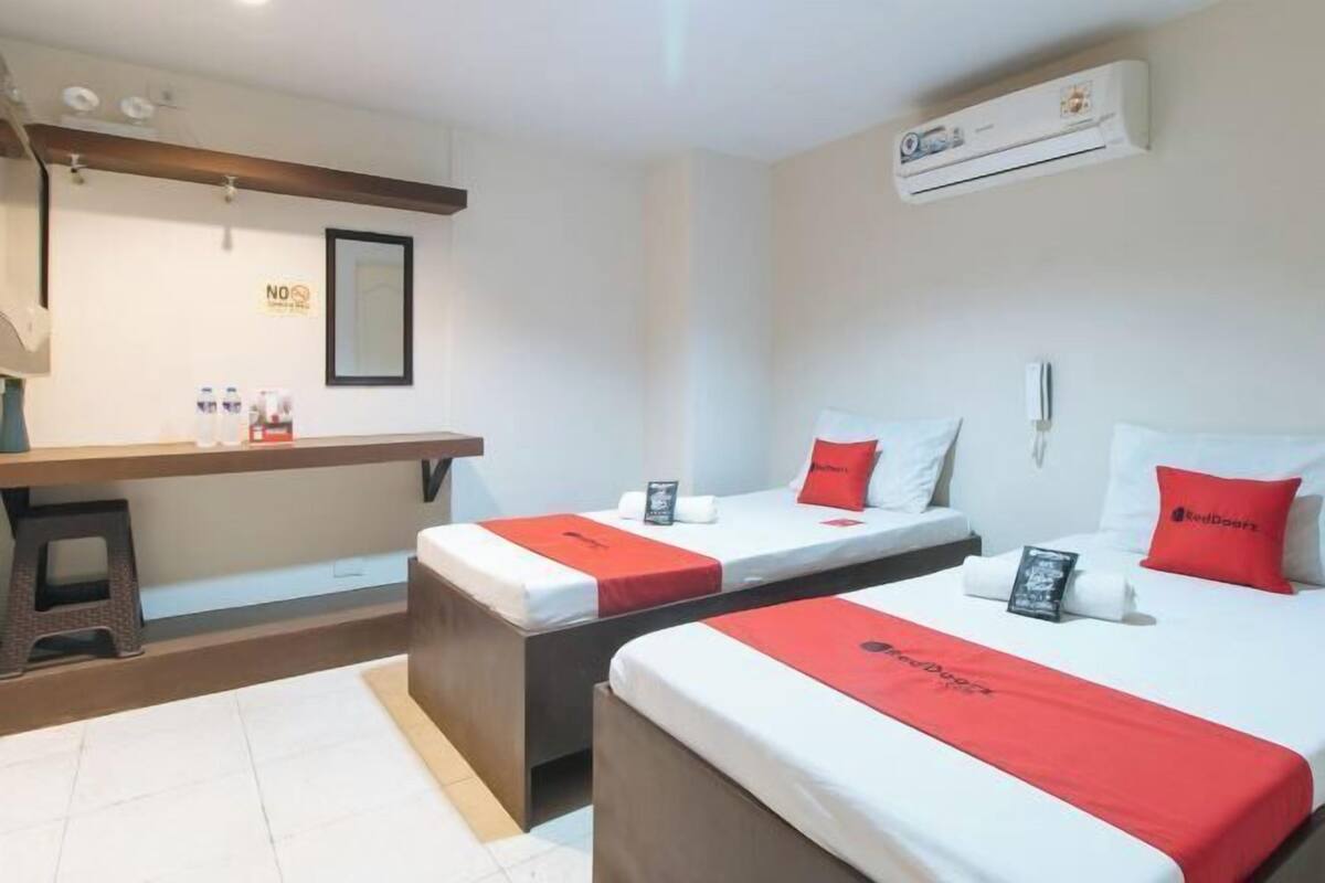 Ein Hotelzimmer mit zwei Betten, einem Schreibtisch und einer Klimaanlage.