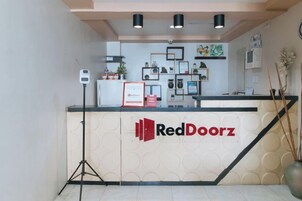 Una zona de recepción con mostrador, un letrero que dice 'RedDoorz' y un trípode con cámara.
