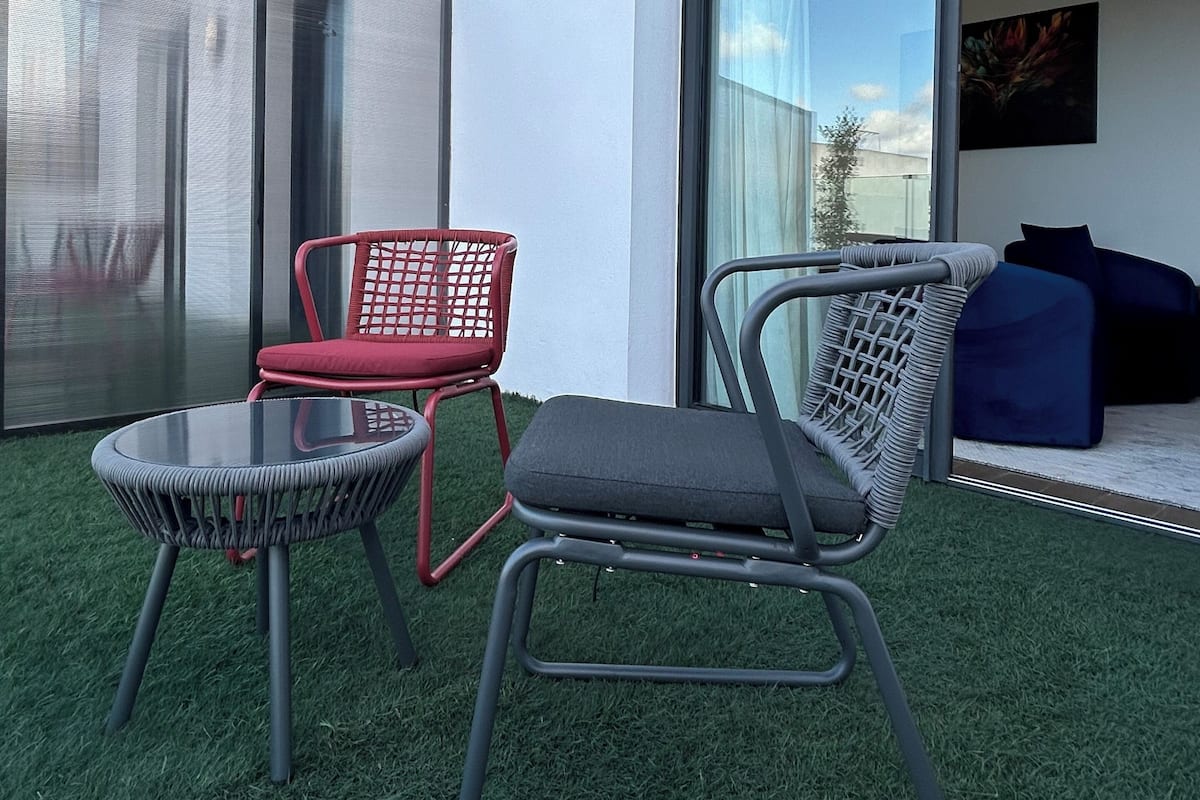A modern outdoor seating area with two chairs and a table, a sliding glass door leading to a living space, and a white exterior wall.