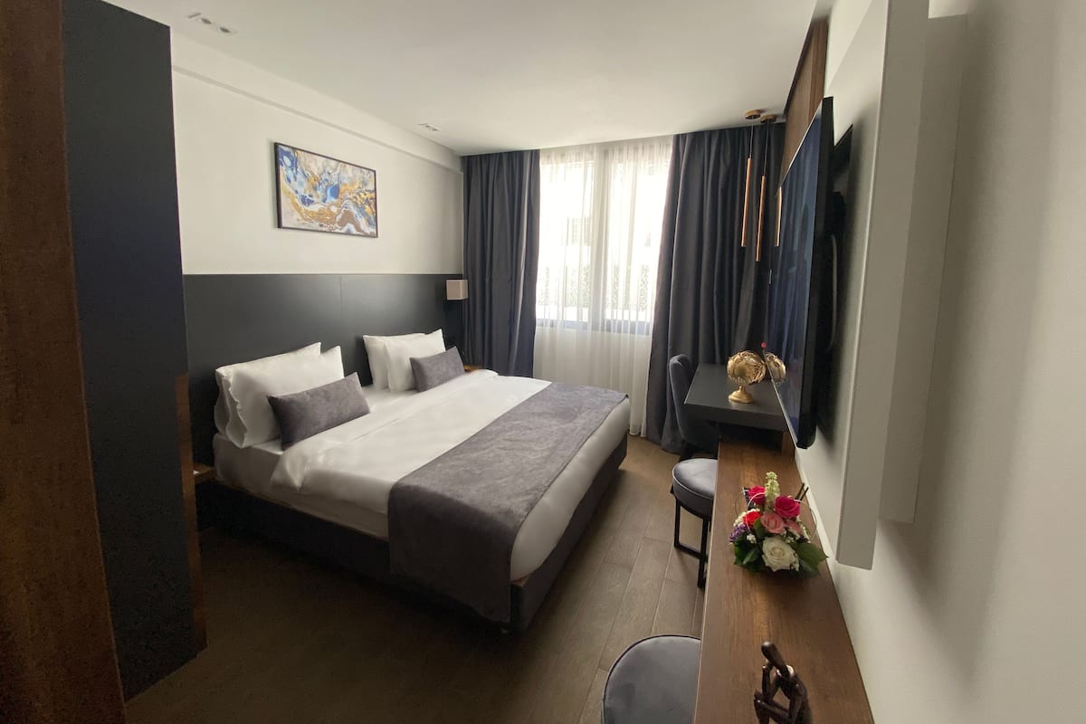 A modern hotel room with a large bed, a desk with a globe and flowers, a TV, and a painting on the wall.