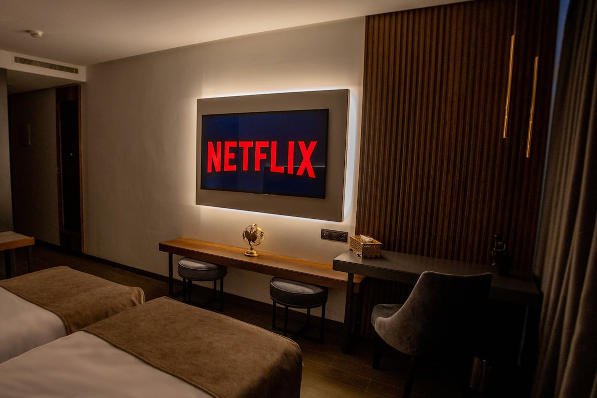 A hotel room with two beds, a desk with a globe, a chair, and a wall-mounted TV displaying "NETFLIX".