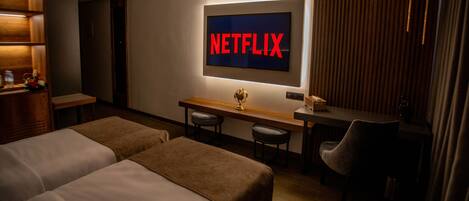 Habitación de hotel con dos camas, un escritorio con un globo terráqueo, una silla y un televisor de pared mostrando “NETFLIX”.