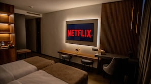 Une chambre d’hôtel avec deux lits, un bureau sur lequel se trouve un globe terrestre, une chaise et un téléviseur fixé au mur qui affiche « NETFLIX ».