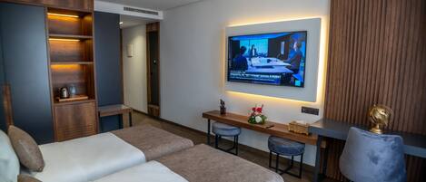 A modern hotel room with a large bed, a desk with two chairs, a television mounted on the wall, and a wooden wardrobe.