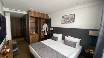 Una camera d'albergo con un letto grande, un armadio, una scrivania con una sedia e un televisore.