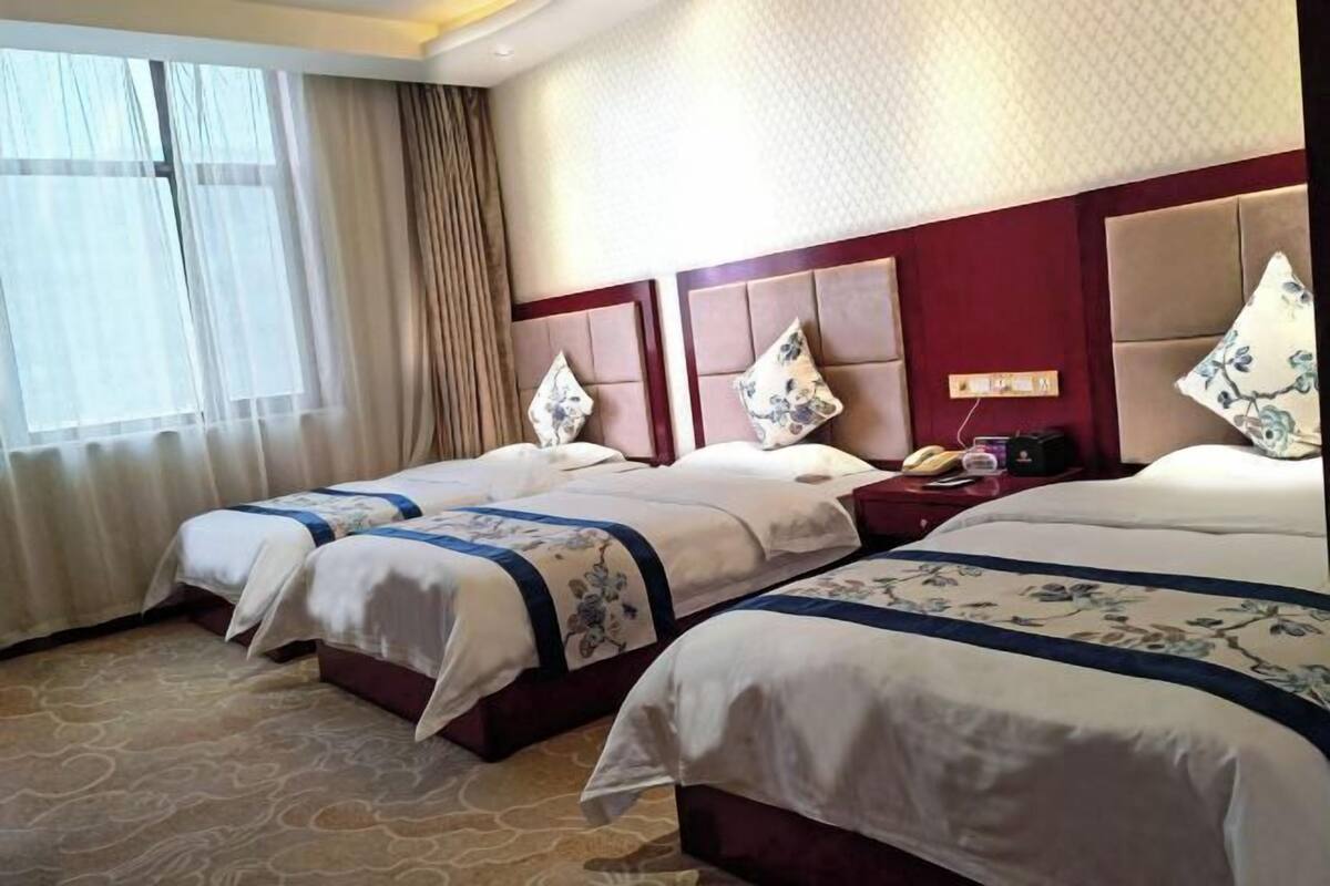 Ein Hotelzimmer mit zwei Betten, einem großen Fenster mit Vorhängen und einer roten Akzentwand.