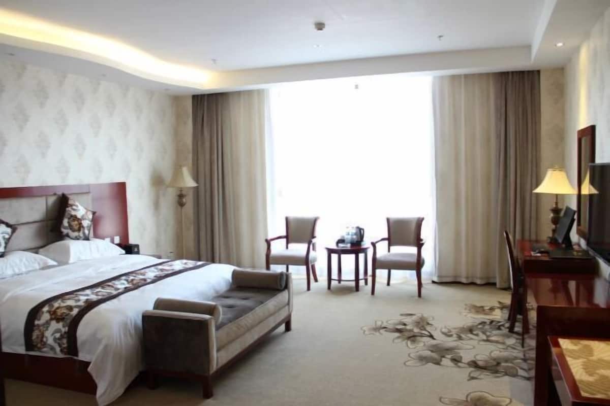 Ein Hotelzimmer mit einem großen Bett, einer Couch, zwei Sesseln, einem kleinen Tisch und einem Fernseher.