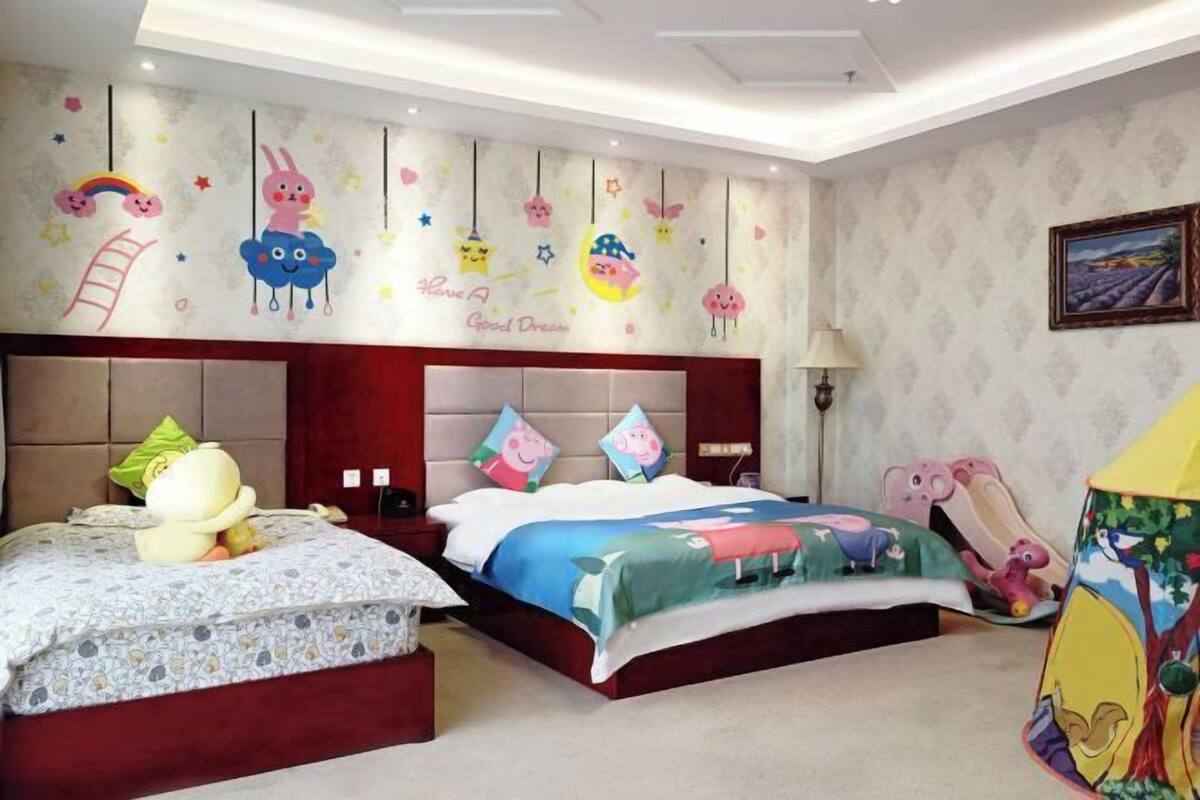 Ein Schlafzimmer mit einem großen Bett, einem kleineren Bett und einem Nachttisch. An den Wänden befinden sich Dekorationen, und auf dem Nachttisch steht eine Lampe.