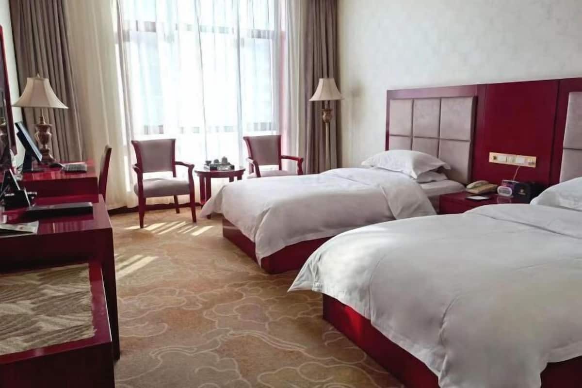 Ein Hotelzimmer mit zwei Betten, einem Schreibtisch mit Lampe, einem Sessel und einem kleinen Tisch.
