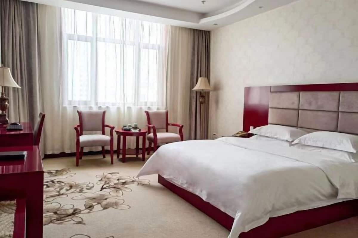 Ein Hotelzimmer mit einem großen Bett, einem Schreibtisch, zwei Stühlen, einem kleinen Tisch und einem Fenster mit Vorhängen.