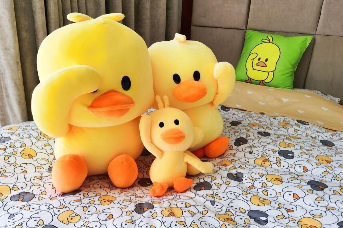A bed with a duck-themed duvet cover and a green pillow with a duck design.