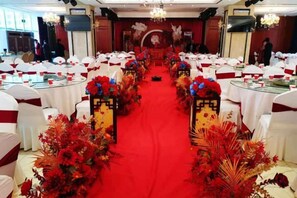 Une salle de banquet avec des tables rondes, une moquette rouge et des centres de table floraux.