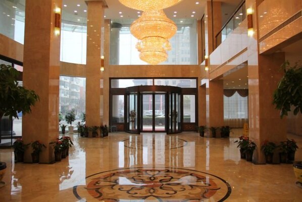 A hotel lobby with a large chandelier, a revolving door, and potted plants.