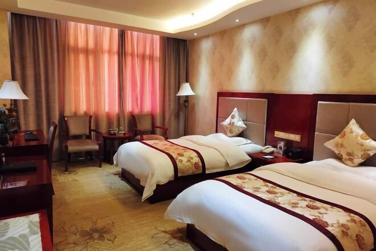 Ein Hotelzimmer mit zwei Betten, einem Schreibtisch, einem Stuhl und einer Lampe.