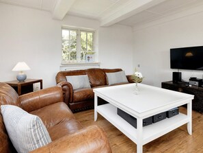 Una sala de estar con un sofá de cuero marrón, una mesa de centro blanca, un televisor y una lámpara.