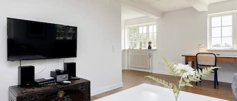 En moderne stue med et fladskærms-tv, en trækommode, et hvidt bord og et vindue med udsigt til grøn natur.