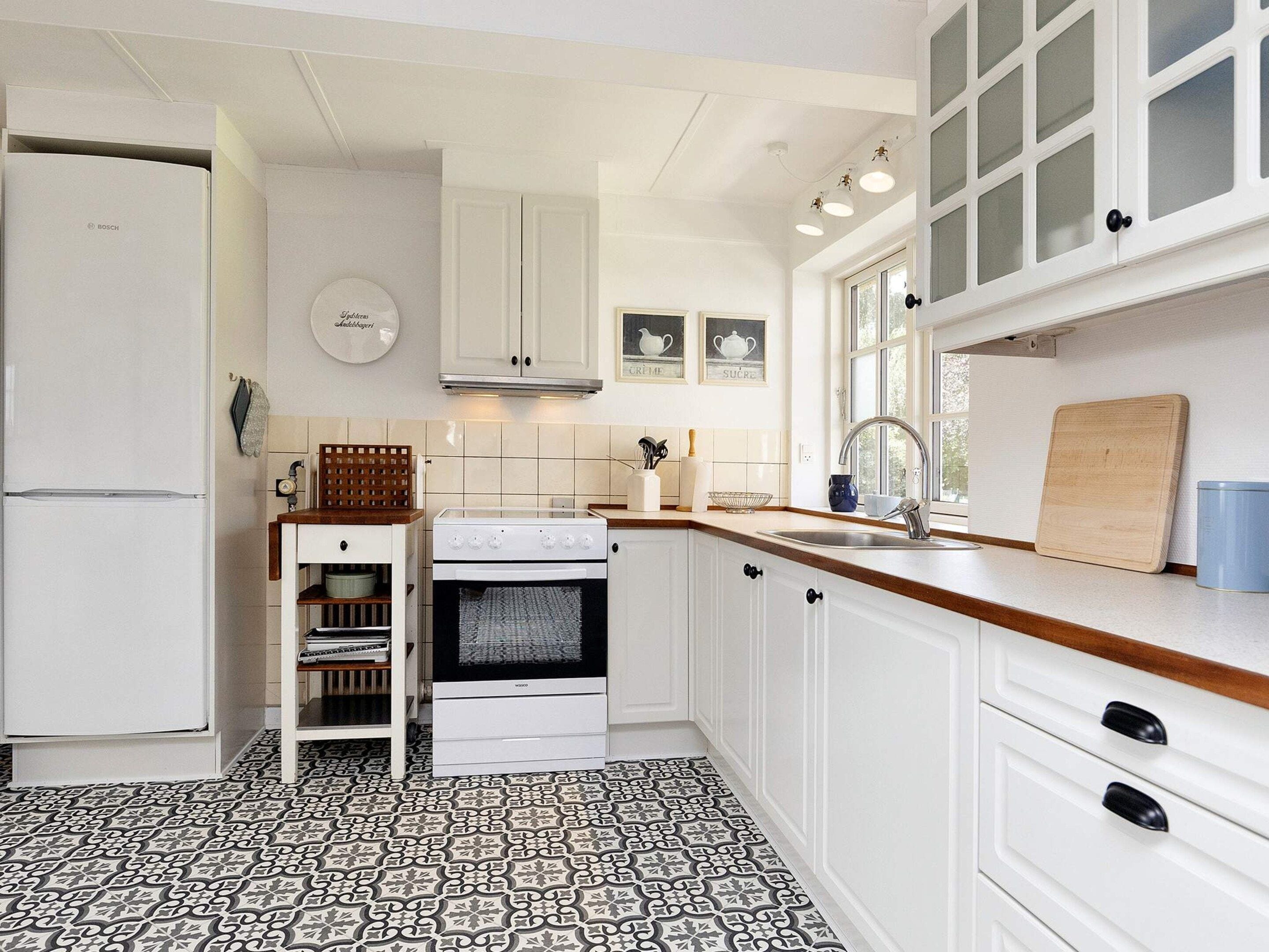 A kitchen with white cabinets, a Bosch refrigerator, a stove, and a window with natural light.