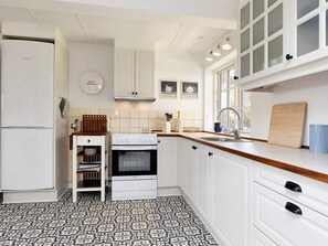A kitchen with white cabinets, a Bosch refrigerator, a stove, and a window with natural light. - 6 Person Holiday Home in Store Heddinge (Store Heddinge)