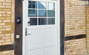 A white door with a window, a brick wall, and a small outdoor area.