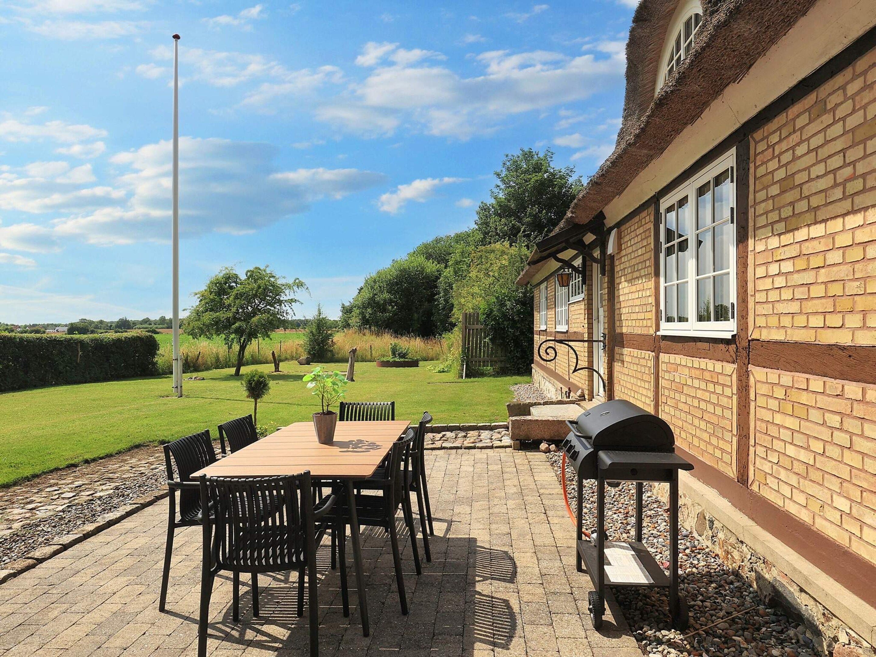 A patio with a table and chairs, a barbecue grill, and a brick building with windows.