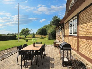 Une terrasse avec une table et des chaises, un barbecue et un bâtiment en briques doté de fenêtres.