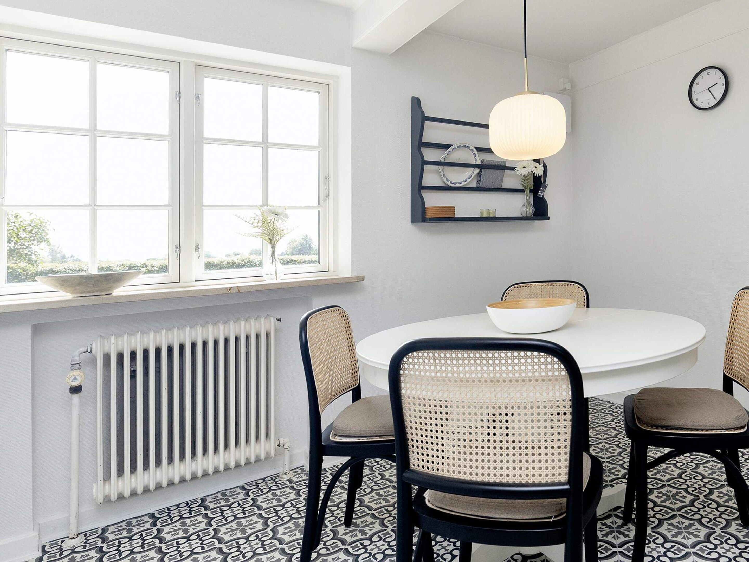 Un comedor con una mesa redonda, cuatro sillas, una lámpara colgante, un reloj de pared y una ventana con vistas.