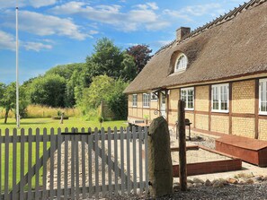 A traditional thatched-roof house with a white picket fence, a stone pillar, and a clear sky.