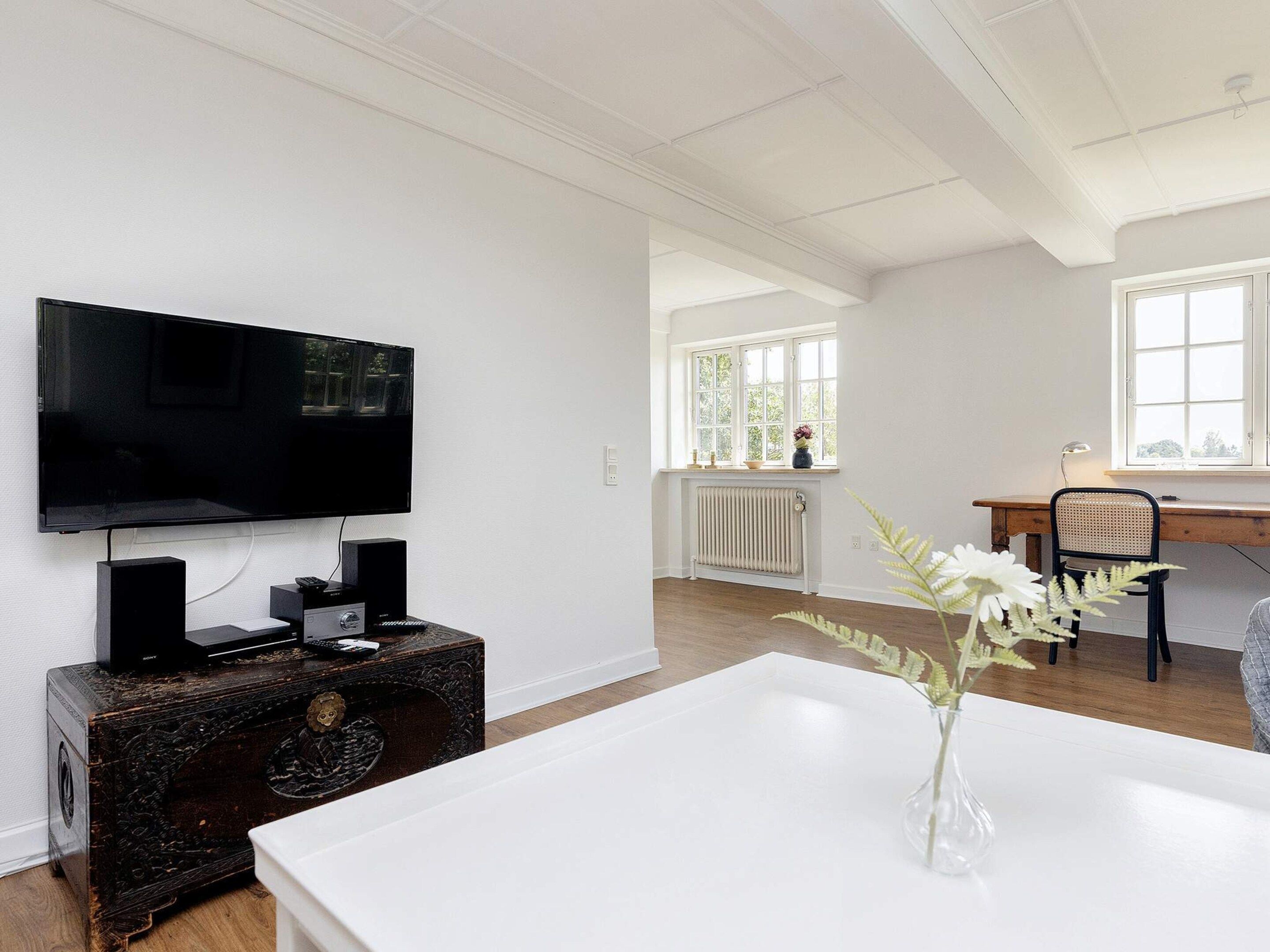 Una sala de estar moderna con un televisor de pantalla plana, una radio antigua y una mesa blanca con un florero.