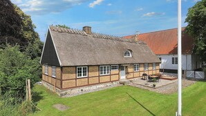 A traditional house with a thatched roof, a stone foundation, and a well-maintained lawn. - 6 Person Holiday Home in Store Heddinge (Store Heddinge)