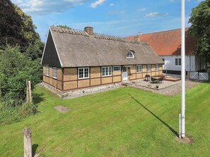 A traditional house with a thatched roof, a stone foundation, and a well-maintained lawn. - 6 Person Holiday Home in Store Heddinge (Store Heddinge)