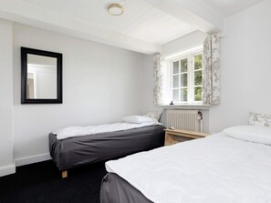 Un dormitorio con dos camas, un radiador, una ventana con cortinas y un espejo en la pared.