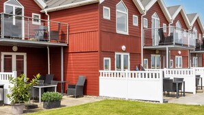 A row of red wooden buildings with balconies, outdoor seating, and a well-maintained lawn. - 6 Person Holiday Home in Hadsund (Hadsund)