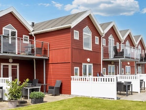 A row of red wooden buildings with balconies, outdoor seating, and a well-maintained lawn. - 6 Person Holiday Home in Hadsund (Hadsund)