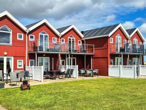 A row of red buildings with balconies, a grassy lawn, and outdoor furniture. - 6 Person Holiday Home in Hadsund (Hadsund)