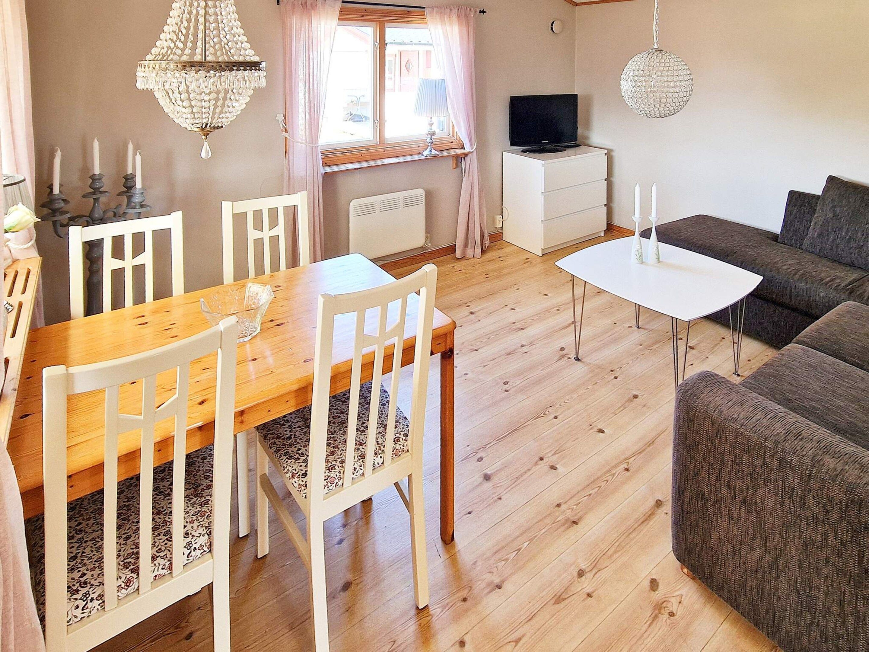 A cozy living room with a wooden dining table, white chairs, a grey sofa, and a TV on a white cabinet.