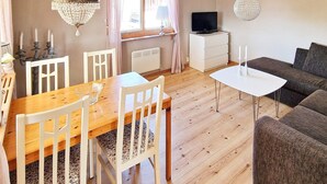 A cozy living room with a wooden dining table, white chairs, a sofa, and a television on a white cabinet. - 5 Person Holiday Home in Skummeslovsstrand (Skummesloevsstrand)
