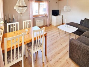 A cozy living room with a wooden dining table, white chairs, a sofa, and a television on a white cabinet. - 5 Person Holiday Home in Skummeslovsstrand (Skummesloevsstrand)