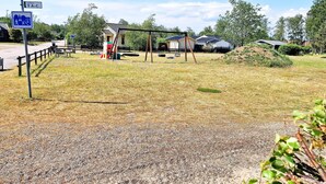 A playground with swings and a slide, a gravel path, and a sign indicating a pedestrian crossing. - 5 Person Holiday Home in Skummeslovsstrand (Skummesloevsstrand)
