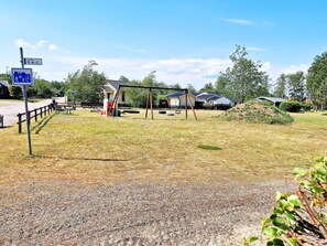 A playground with swings and a slide, a gravel path, and a sign indicating a pedestrian crossing. - 5 Person Holiday Home in Skummeslovsstrand (Skummesloevsstrand)