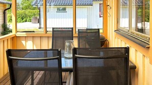 A covered outdoor seating area with a table and chairs, a view of a house in the background, and a window on the right side. - 5 Person Holiday Home in Skummeslovsstrand (Skummesloevsstrand)