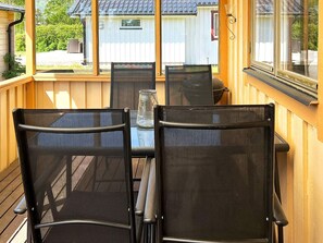 A covered outdoor seating area with a table and chairs, a view of a house in the background, and a window on the right side. - 5 Person Holiday Home in Skummeslovsstrand (Skummesloevsstrand)